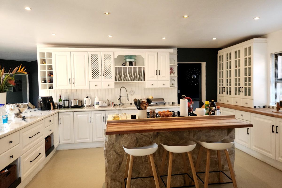 Spacious kitchen featuring white cabinetry, marble-look countertops, a stone-clad island with a wooden breakfast bar, and ample storage with glass-fronted display units.
