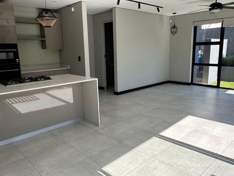Modern open-plan living area featuring a sleek kitchen with a central island, gas hob, built-in oven, and large sliding doors leading to the garden.