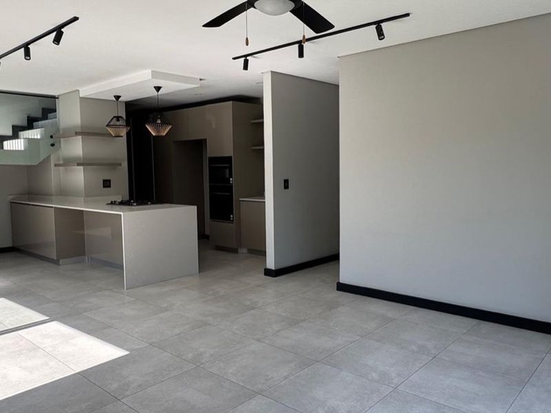 Modern open-plan living area featuring a sleek kitchen with island, built-in appliances, and a contemporary staircase with glass balustrade.