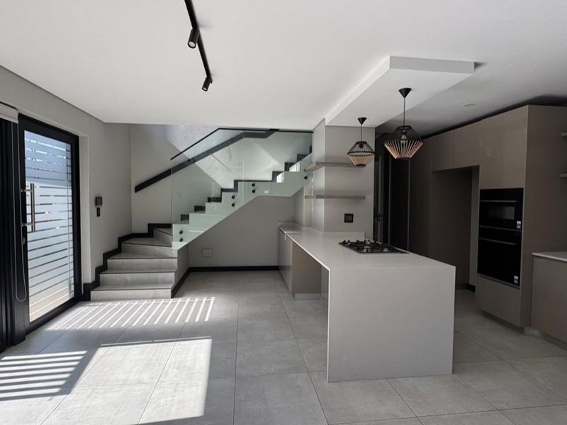 Modern open-plan kitchen featuring a central island with gas hob, built-in appliances, sleek cabinetry, and a striking staircase with glass balustrades.