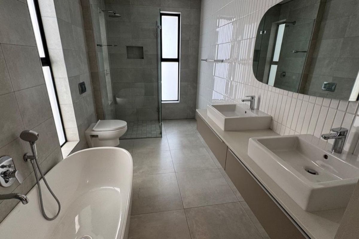 Modern bathroom featuring a double vanity, freestanding bathtub, walk-in shower, and wall-mounted toilet with contemporary grey and white tiling.