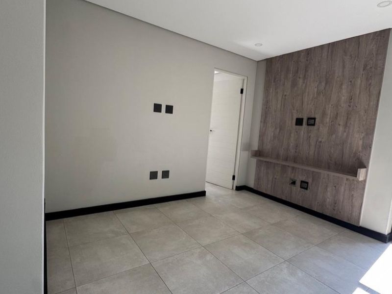 Modern bedroom featuring large format floor tiles, a wood-look feature wall with a built-in shelf, and recessed lighting.