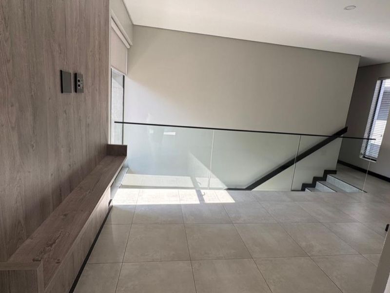 A modern, spacious landing area featuring a glass balustrade, tiled flooring, and a contemporary wood-paneled feature wall with a built-in floating shelf.