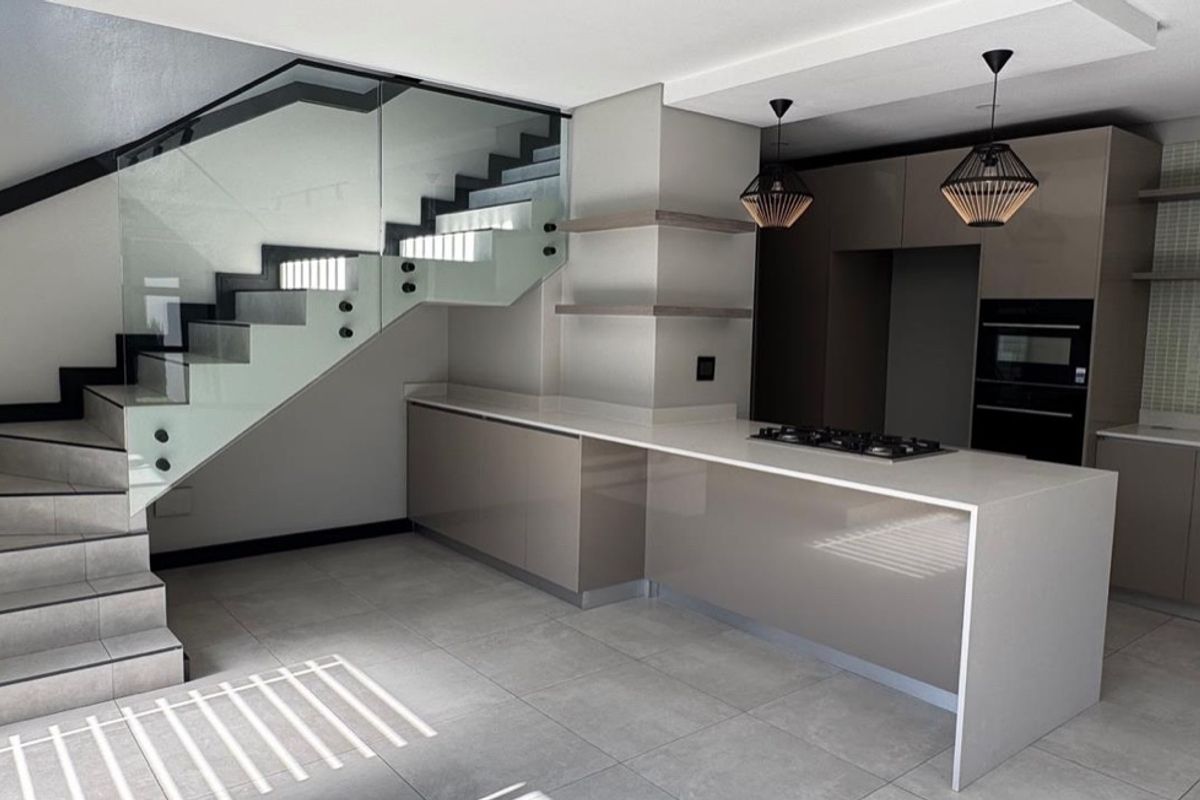 Modern kitchen featuring sleek cabinetry, stone countertops, integrated gas hob and oven, complemented by a striking glass balustrade staircase.