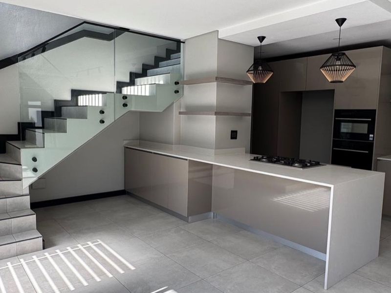 Modern kitchen featuring sleek cabinetry, stone countertops, integrated gas hob and oven, complemented by a striking glass balustrade staircase.