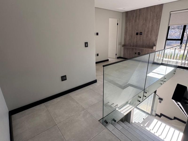 Modern upper-level landing area featuring sleek glass balustrades, large format floor tiles, and a contemporary wood-look feature wall.