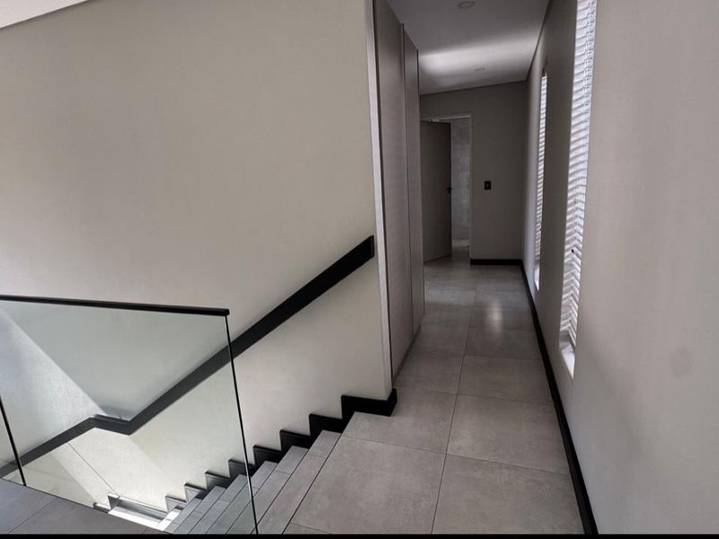 A modern, well-lit hallway featuring tiled flooring, a sleek glass balustrade staircase, and built-in storage cupboards.
