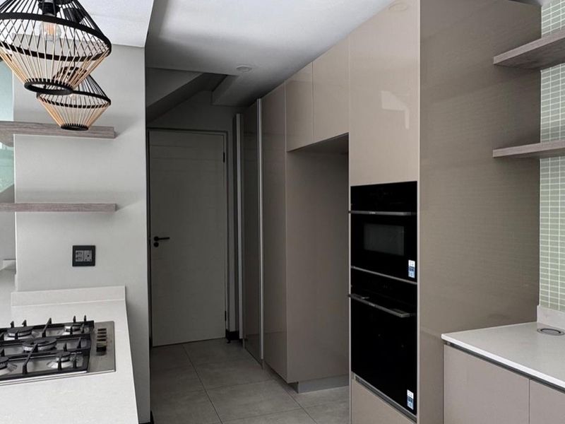 Modern kitchen featuring high-gloss cabinetry, stone countertops, integrated oven and microwave, gas hob, and stylish floating shelves with a tiled backsplash.