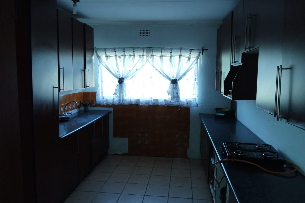 A galley-style kitchen featuring dark cabinetry, gas hob, and tiled flooring. The space requires cosmetic updates and improved lighting to enhance its functionality.