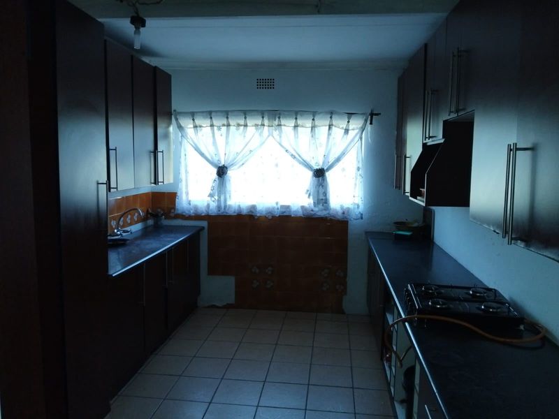 A galley-style kitchen featuring dark cabinetry, gas hob, and tiled flooring. The space requires cosmetic updates and improved lighting to enhance its functionality.