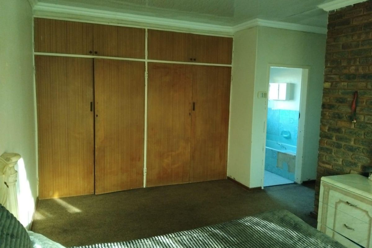 Bedroom featuring built-in wooden cupboards, a brick feature wall, and direct access to an en-suite bathroom with dated finishes.