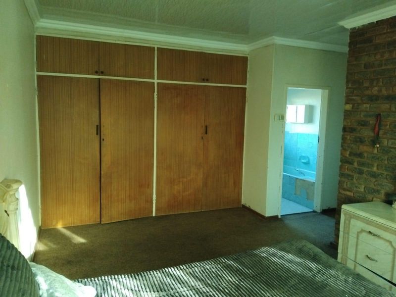 Bedroom featuring built-in wooden cupboards, a brick feature wall, and direct access to an en-suite bathroom with dated finishes.