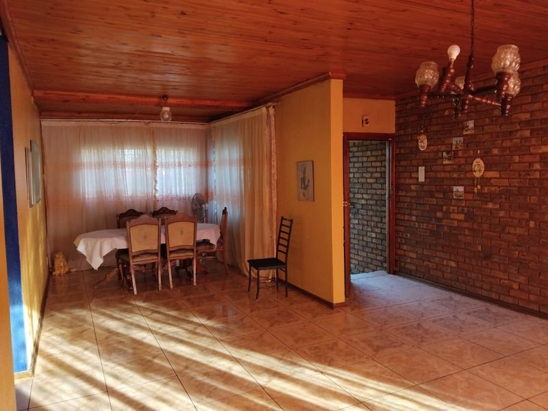 Spacious living area featuring an exposed timber ceiling, ceramic floor tiles, and a rustic exposed brick feature wall.