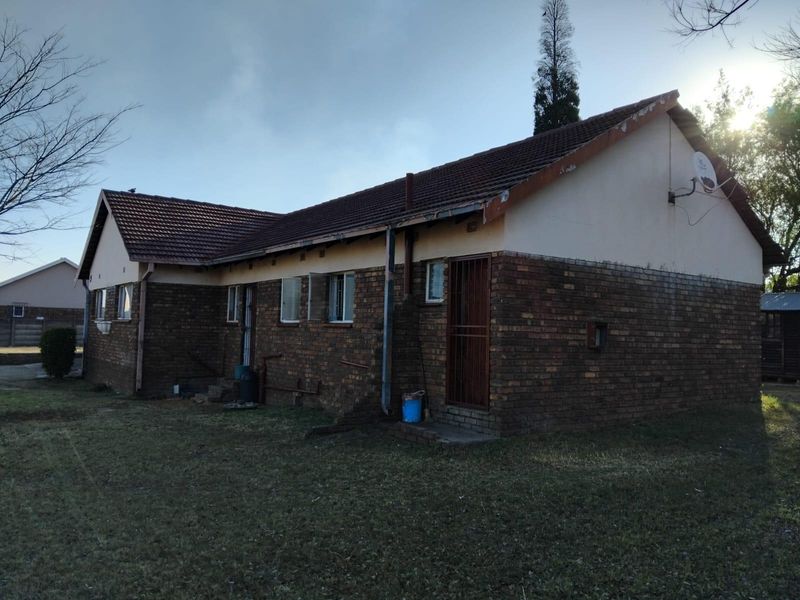 Rear view of a single-story face-brick house featuring a tiled roof and security gate access.