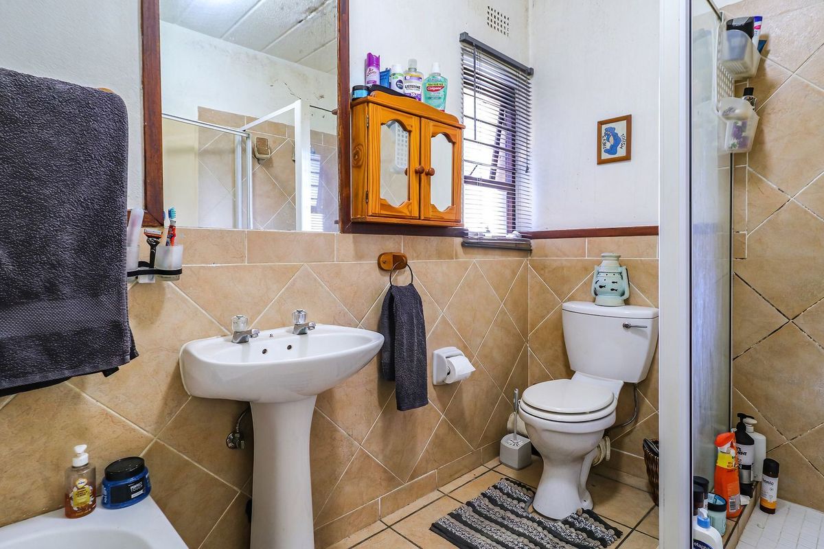 A functional bathroom featuring a pedestal basin, toilet, and shower enclosure with tiled finishes, requiring some cosmetic updates to the ceiling and wall tiles.