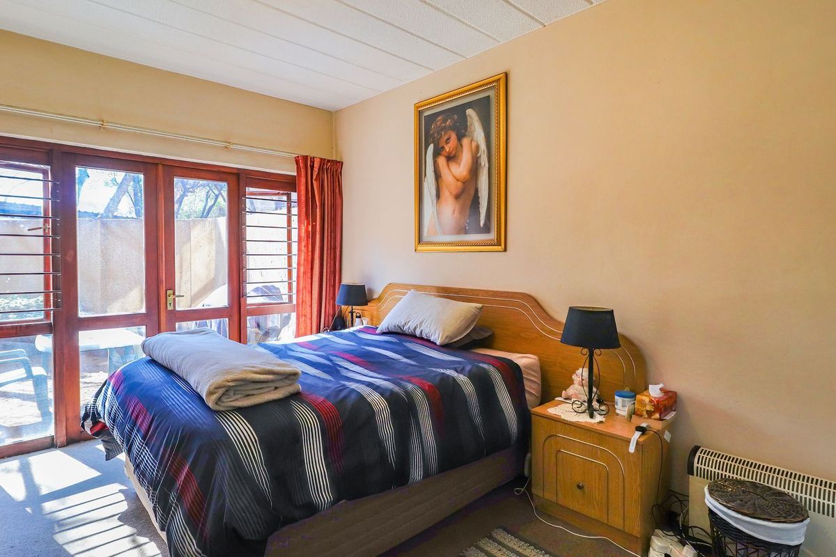 A bedroom featuring timber-framed glass sliding doors with security bars, providing natural light and access to the exterior.