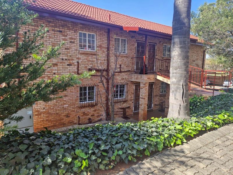 Rear view of a double-story face brick townhouse featuring a tiled roof, security gates, and an external staircase leading to the upper level.