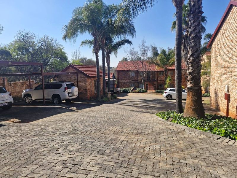 Front view of the townhouse complex featuring a paved driveway, covered carport parking, and established facebrick buildings with tiled roofs.