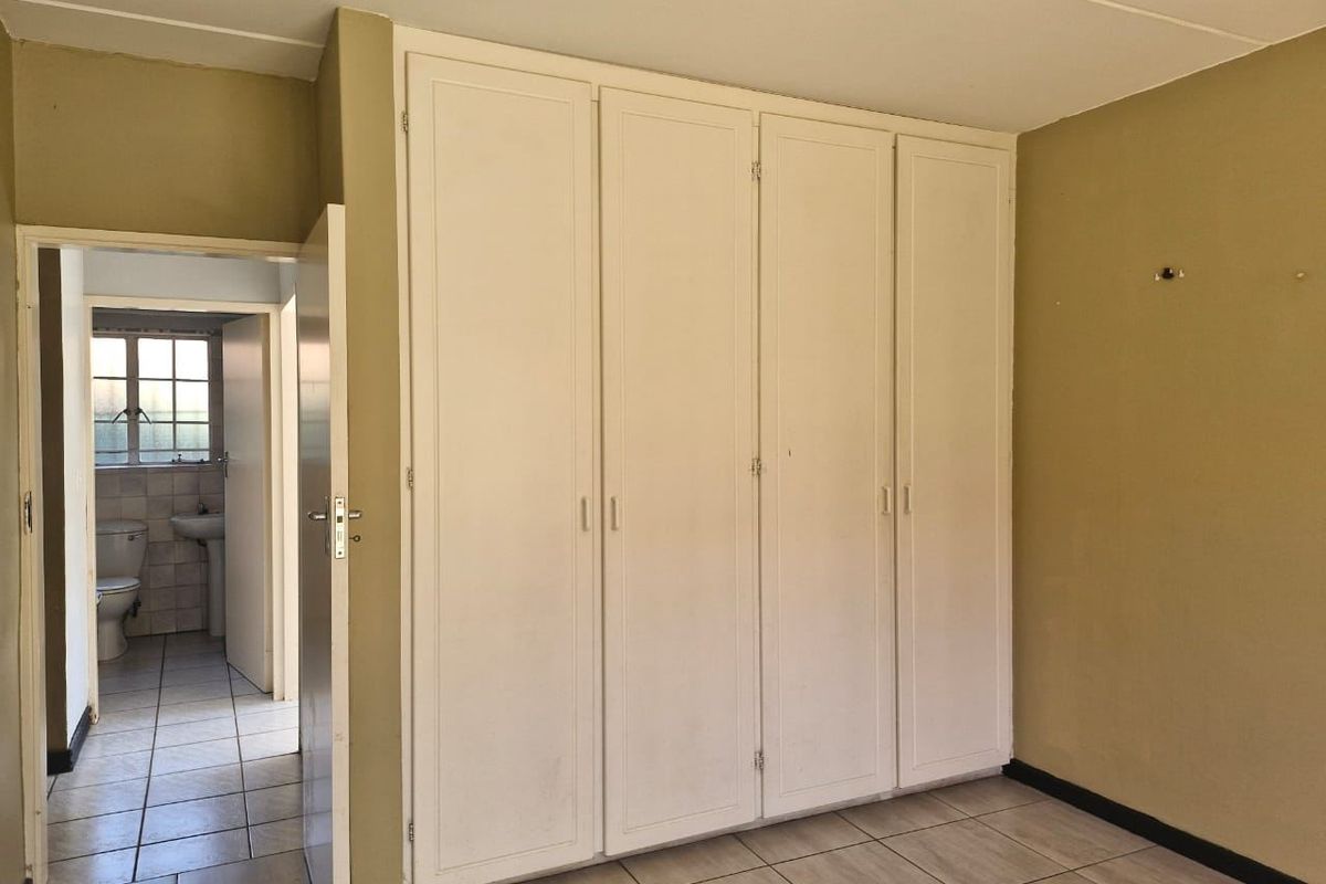 A vacant bedroom featuring built-in cupboards, tiled flooring, and an adjacent view into a bathroom.