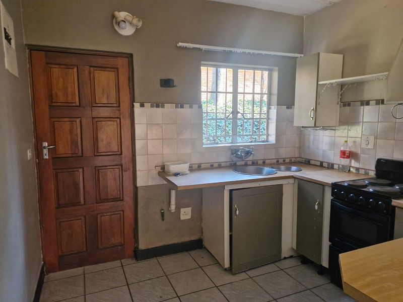 A functional kitchen featuring tiled flooring, a stainless steel sink, built-in cabinetry, and a freestanding stove, with potential for cosmetic updates.