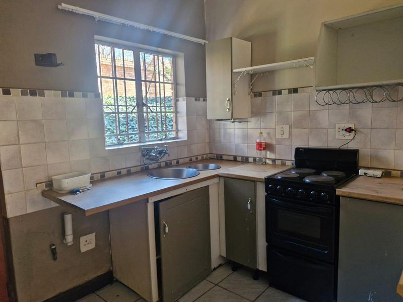 A compact kitchen featuring a double bowl sink, tiled splashback, and freestanding stove, requiring some cosmetic updates and repairs to cabinetry and finishes.