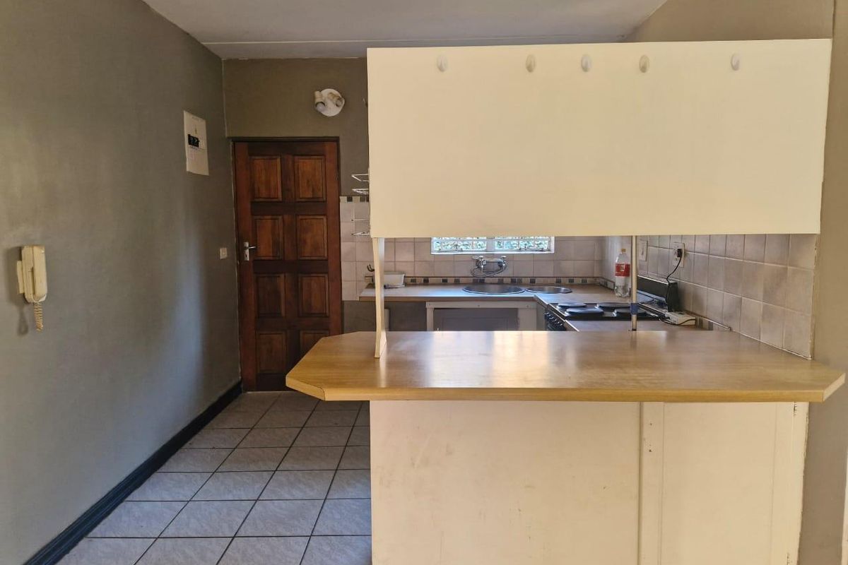 A functional kitchen area featuring a breakfast bar, tiled backsplash, built-in hob, and tiled flooring, offering a blank canvas for modern renovation.
