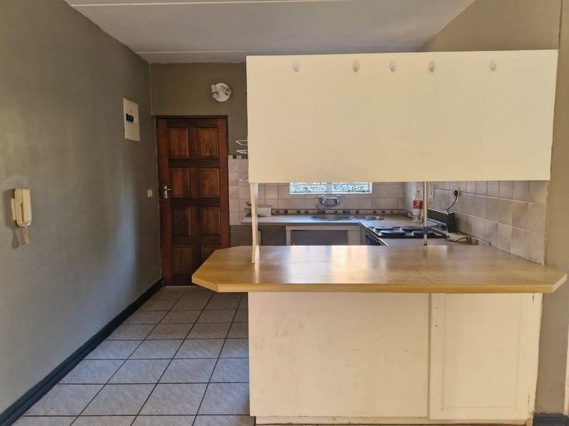 A functional kitchen area featuring a breakfast bar, tiled backsplash, built-in hob, and tiled flooring, offering a blank canvas for modern renovation.