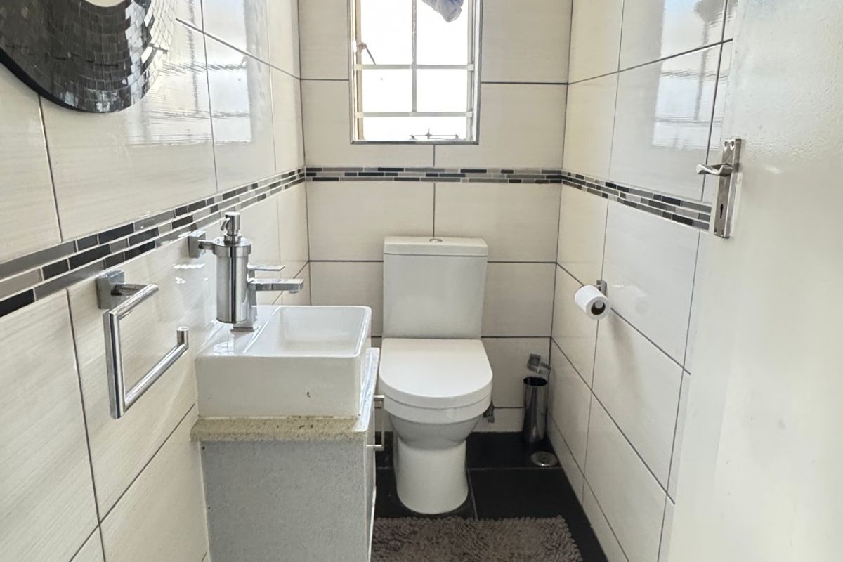 A compact, modern guest bathroom featuring floor-to-ceiling wall tiles, a wall-mounted vanity basin, and dark slate flooring.