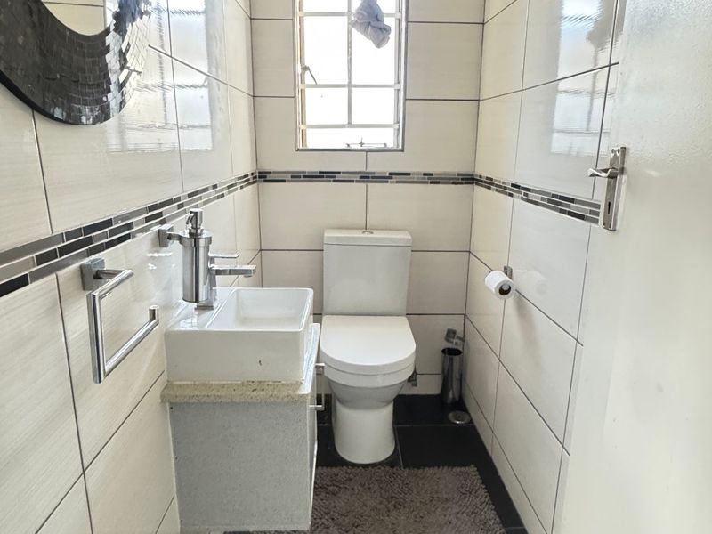 A compact, modern guest bathroom featuring floor-to-ceiling wall tiles, a wall-mounted vanity basin, and dark slate flooring.