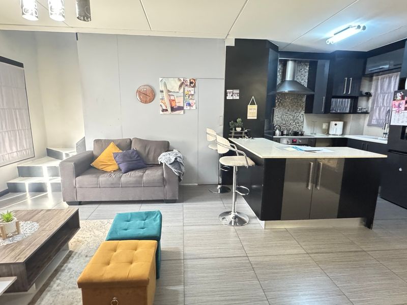Open-plan living area featuring a modern kitchen with a central island, breakfast bar, and tiled flooring, seamlessly connected to the lounge space.