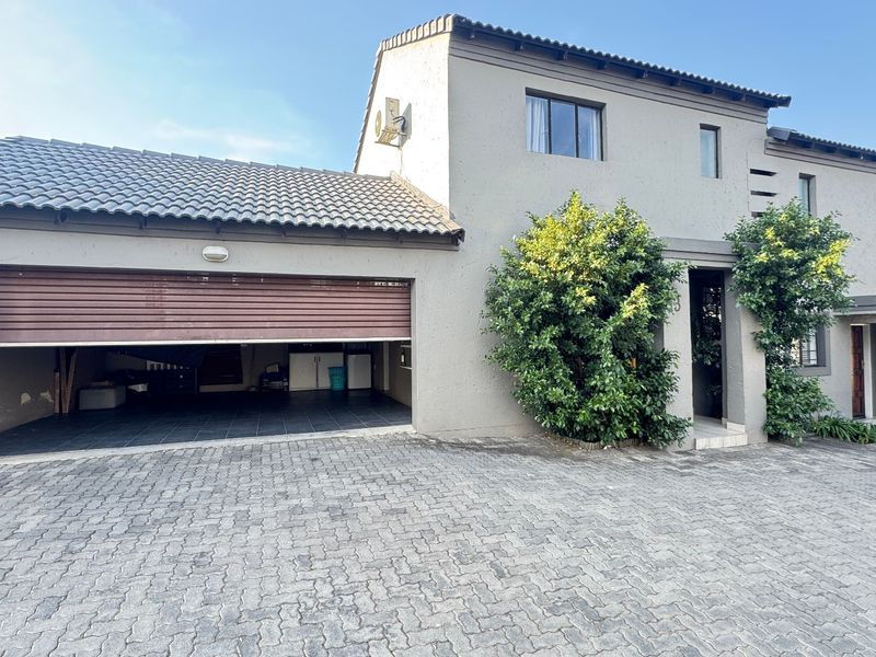 Front elevation of a townhouse featuring a paved driveway, double garage with a roller door, and a neutral rendered facade.