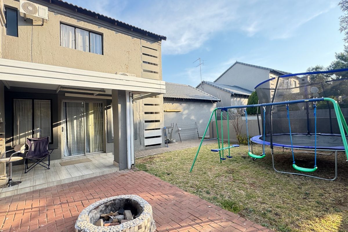 Rear exterior view of the townhouse featuring a covered patio, brick paved area with a built-in fire pit, and a private garden space.