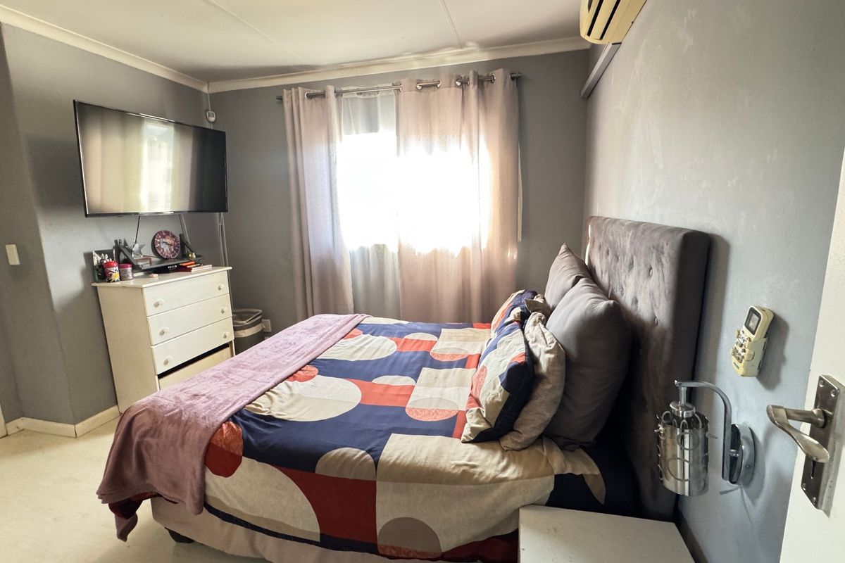 A functional bedroom featuring a wall-mounted air conditioning unit, coving, and a wall-mounted light fixture, with direct access to an en-suite bathroom.