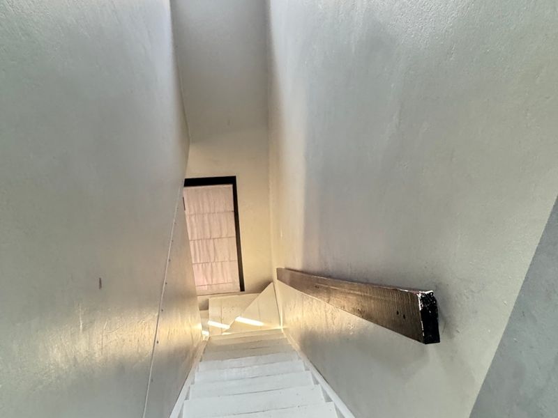 A narrow interior staircase featuring a skylight and a wooden handrail, leading down to a lower level.