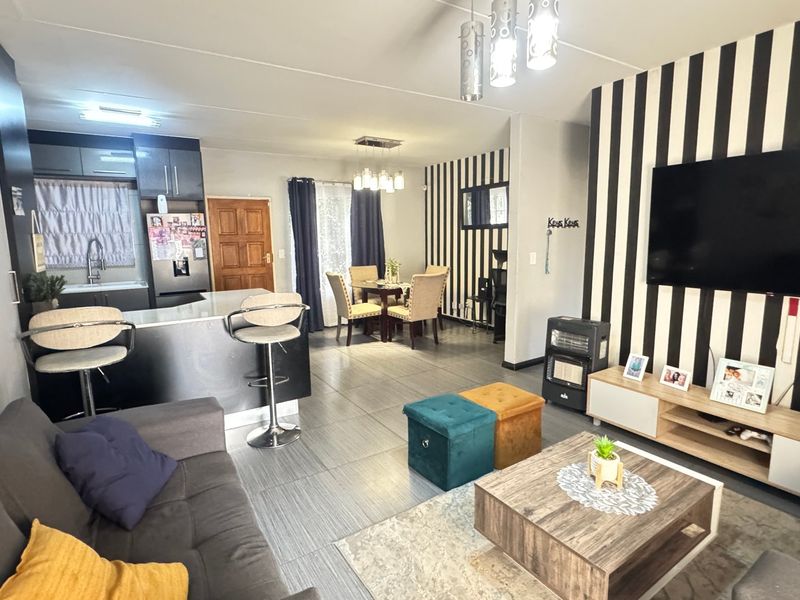 Open-plan living area featuring a kitchen with island, dining space, and lounge area with tiled flooring and modern pendant lighting.