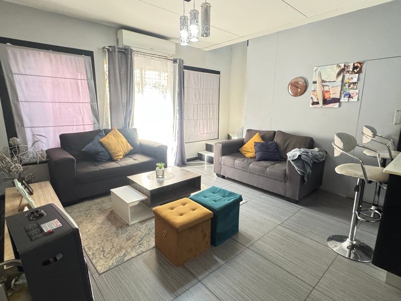 Open plan living area featuring tiled flooring, a breakfast bar, and an integrated air conditioning unit, providing a functional and connected living space.