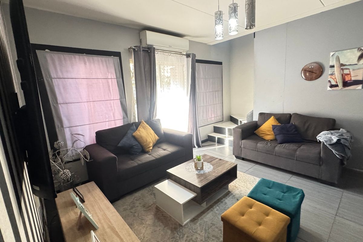 A comfortable living room featuring tiled flooring, a split-system air conditioner, and a staircase leading to the upper level.
