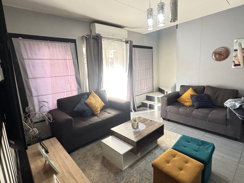 A comfortable living room featuring tiled flooring, a split-system air conditioner, and a staircase leading to the upper level.