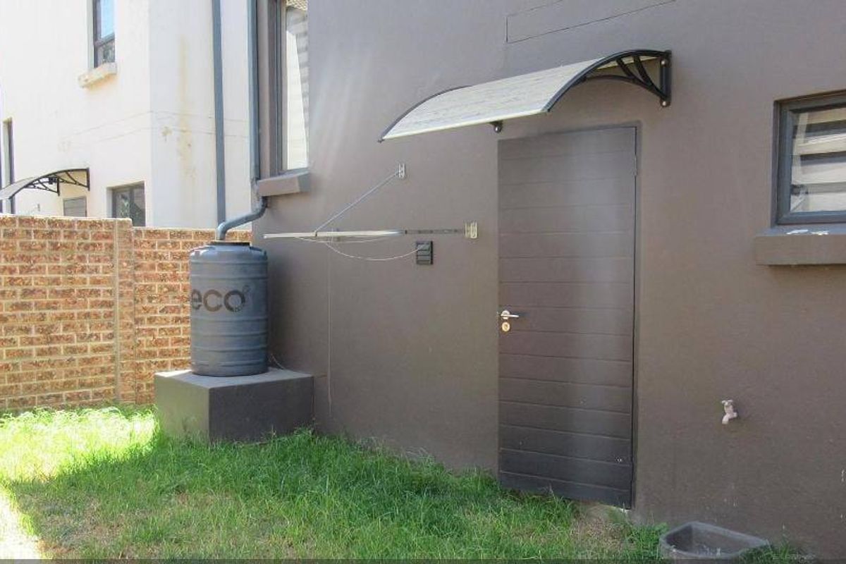 Rear exterior view showing a brick boundary wall, water tank, and a side access door with a protective awning.