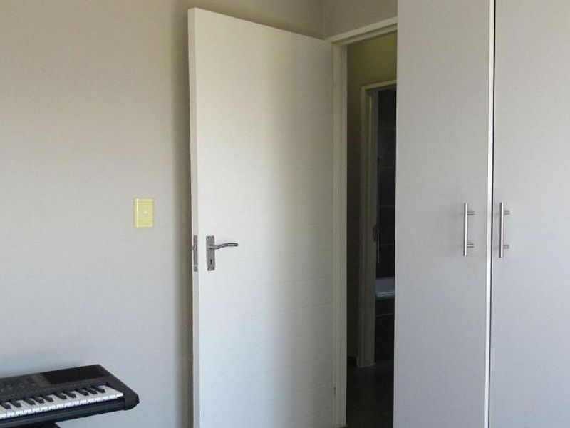 A clean bedroom interior featuring neutral walls, built-in cupboards, and a doorway leading to an adjacent room.