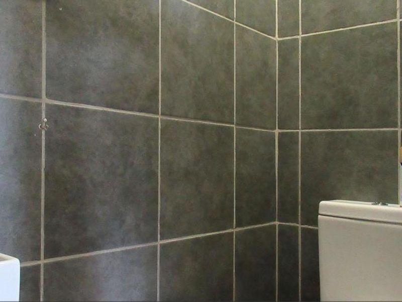 A compact bathroom featuring dark grey ceramic wall tiles, a standard toilet, and a small washbasin.