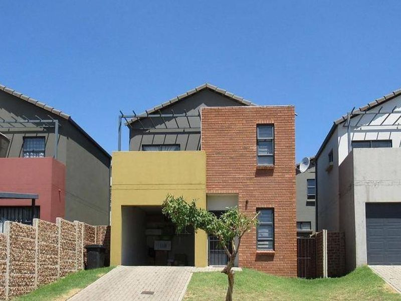 A row of modern multi-story residential townhouses featuring brick facades, paved driveways, and integrated garage structures under a clear blue sky.