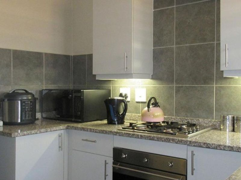 A functional kitchen featuring granite countertops, a built-in oven with gas hob, tiled backsplash, and ample fitted cabinetry with under-cabinet lighting.