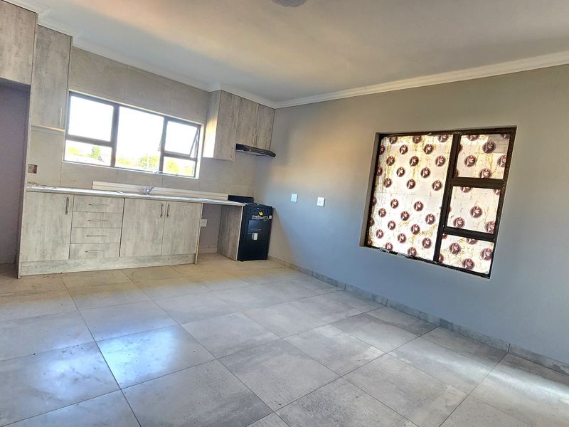 Open-plan kitchen and living area featuring modern light wood-look cabinetry, tiled flooring, and large windows providing ample natural light.