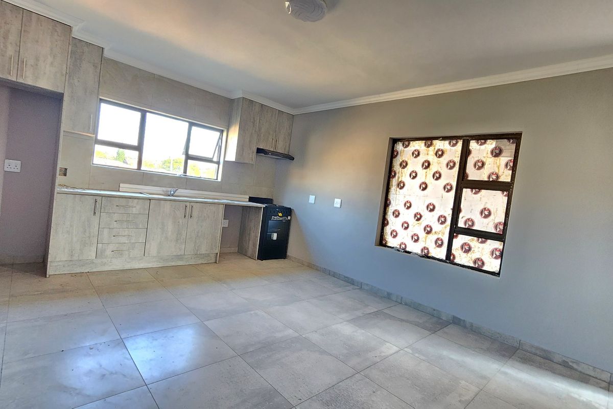 An open-plan kitchen and living area featuring modern light-wood cabinetry, tiled flooring, and neutral wall finishes in a clean, vacant space.