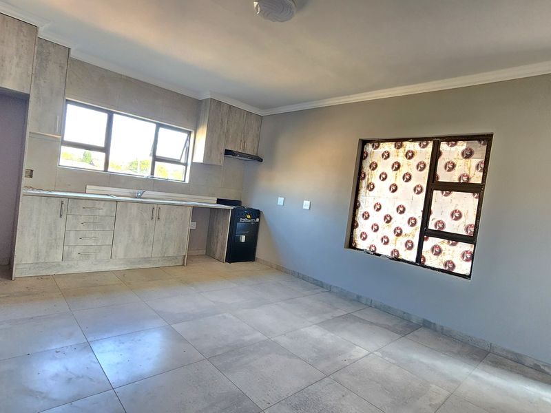 An open-plan kitchen and living area featuring modern light-wood cabinetry, tiled flooring, and neutral wall finishes in a clean, vacant space.