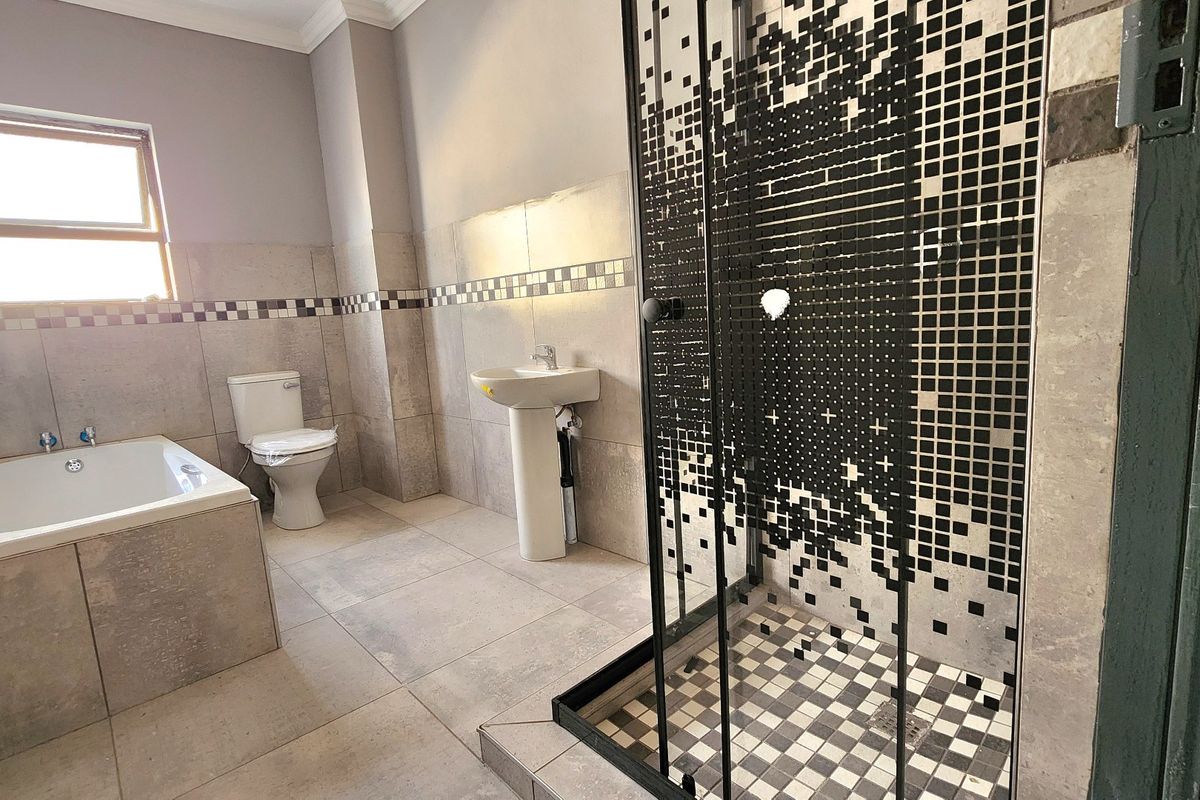 A modern bathroom featuring a built-in bathtub, pedestal basin, toilet, and a walk-in shower with a distinctive black and white mosaic tile design.