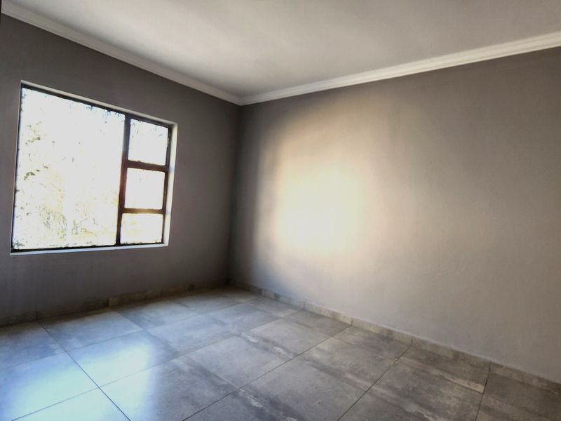 A bright, empty bedroom featuring neutral grey walls, large tiled flooring, and a clean cornice finish, ready for personalization.