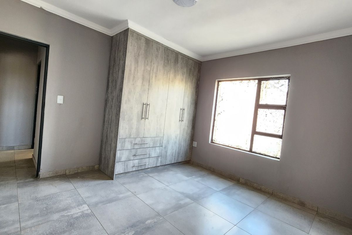 A bright, empty bedroom featuring modern grey-toned built-in cupboards, neutral wall paint, and large format floor tiles.