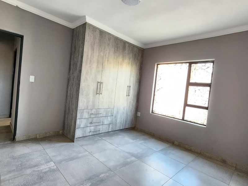 A bright, empty bedroom featuring modern grey-toned built-in cupboards, neutral wall paint, and large format floor tiles.